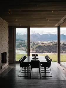 An elegant dining room with large windows showcasing a picturesque mountain landscape, featuring modern black wooden table an