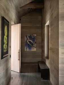 A modern entryway featuring wooden walls and a door, with abstract artwork and a bench.