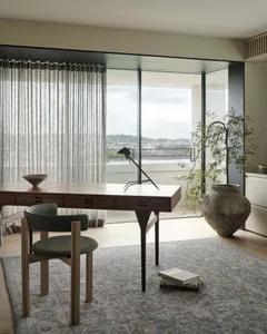 A modern home office with a wooden desk, green chair, and large window overlooking a city.