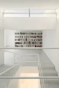Modern white-shelved library with concrete floor and large glass window.