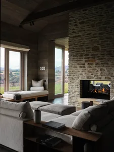 Modern living room featuring a stone fireplace and wood-paneled walls, with a view of the landscape beyond the large windows.