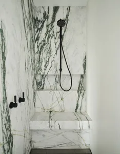 A modern bathroom featuring marble walls and steps with a black showerhead and fixtures.