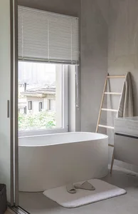 Modern minimalist bathroom with a concrete bathtub, white blinds, and a ladder for towels.