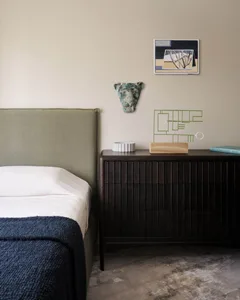 A minimalist bedroom featuring wooden furniture, a green headboard, and a side table with decorative items.