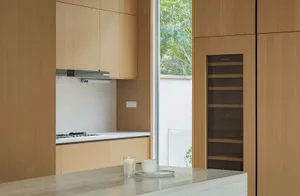 A modern, minimalist kitchen with wooden cabinets, a marble countertop, and a view of the outdoors.