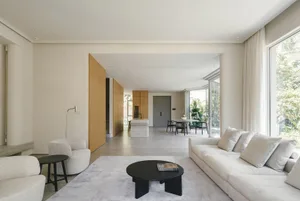 Modern, minimalist living room with concrete flooring, white furniture, and large windows.