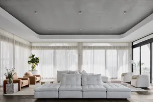 Modern minimalist living room featuring a large white fabric sofa, a beige armchair, and a glass coffee table, with large win