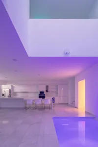 Modern minimalist kitchen with white marble countertops and a pool area with purple lighting.
