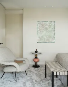 A modern living room featuring a monochromatic color palette with a white armchair, a woven bench, and an abstract painting o