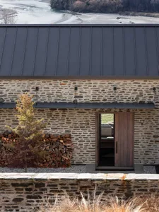 Modern residential stone cabin with a metal roof and a wooden door.