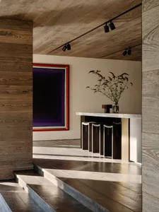 Modern residential interior with wooden flooring, a minimalist bar area with stools, and a large colorful artwork on the wall