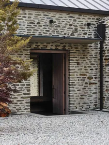 A building entrance made of stone with a wooden door and gravel pathway.