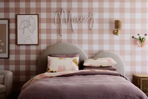 A minimalist bedroom featuring light pink and white checkered wallpaper, a cozy bed with floral-patterned cushions, and a han