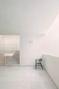 A minimalist interior with white walls, marble floor, and a single chair.