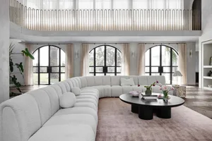 Modern living room with a large curved sofa, glass windows, and a black coffee table with flowers.