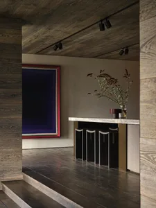 A modern interior space featuring dark wooden walls and floor, with a colorful abstract painting and a small vase with greene