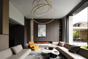 A modern living room with marble, glass, and wooden elements, featuring a fireplace, couches, and a contemporary chandelier.