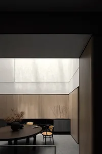 A minimalist dining room featuring a round wooden table, cane-back chairs, a glass chandelier, and a modern artwork on a conc