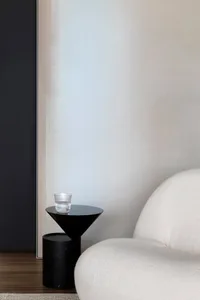 A minimalistic living room featuring a sleek, modern white sofa and a black side table with a single glass tumbler.