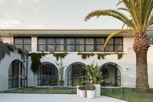 Modern residential exterior with white render, greenery, and palm trees.