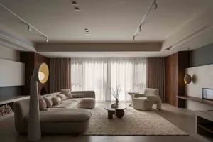 A modern, neutral-toned living room with a couch, armchair, and rug.