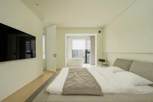 Modern minimalist bedroom featuring a bed with a fabric headboard, wooden floor, and glass window