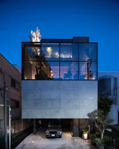A minimalist house with a concrete base and glass walls at night.