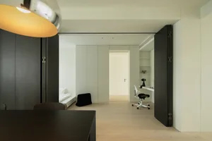 A minimalist office space featuring light wood flooring and white panel walls.