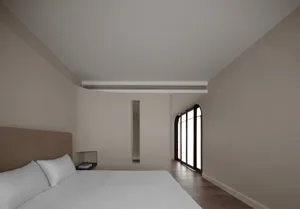 A minimalist bedroom with a white bed, wooden floor, and glass window.