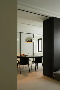 A modern minimalist dining room featuring a metallic pendant light fixture, black chairs, and a wooden floor.