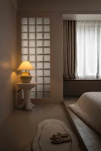 A minimalist bedroom featuring a glass-block wall and a bed with beige textiles.