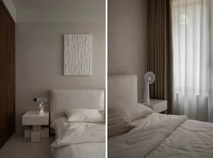 A minimalist bedroom with a white fabric bed, white bedding, and beige curtains. Simple nightstand and abstract artwork on th