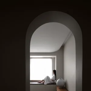 女子坐在窗台上，置身於極簡室內空間，牆面與窗戶皆為中性色調。