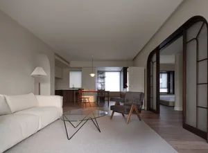 Minimalist living room featuring neutral-toned furniture and flooring, with a modern coffee table and armchair.