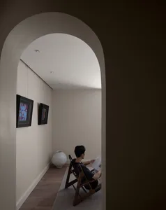 A minimalist reading room with a wooden chair and a white vase, featuring two framed artworks on the wall.