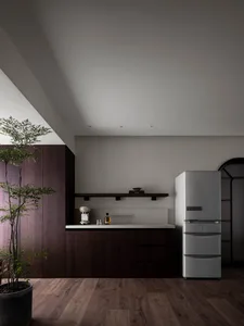 A modern kitchen featuring dark wooden cabinets, a white countertop, and a sleek refrigerator, with a potted plant nearby.