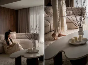 A modern lounge room with velvet cushions, white curtains, a bamboo branched plant, and a table.