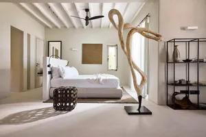 A minimalist bedroom featuring a bed with neutral bedding, a large abstract sculpture, and a modern bookshelf.