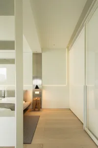 Modern minimalist bedroom with white walls, wooden flooring, and simple furniture arrangement.