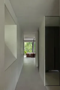 A minimalist modern hallway with concrete walls and glass windows, featuring a view of greenery outside.