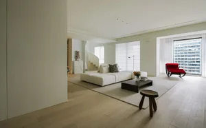 A minimalist living room with a white marble floor, white modular sofa, and red accent chair.
