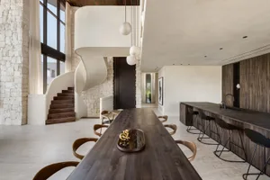 Modern residential kitchen featuring a long wooden table with a decorative gold object, a spiral staircase, and a bar counter