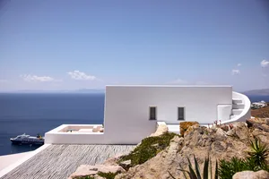 A modern residential building with white stucco walls and a curved stone pathway, overlooking the ocean.