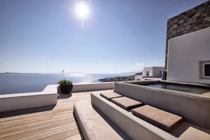 A vacation home with a wooden deck, stone walls, and a concrete pool overlooking the ocean.