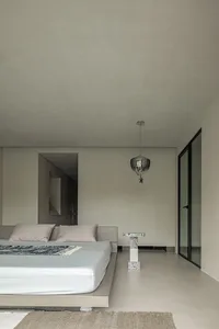 Minimalist bedroom featuring a concrete platform bed with a textured rug and a contemporary pendant light hanging above it.