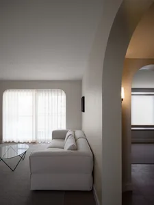 A minimalist living room with a white textured sofa, arched windows, and soft lighting.