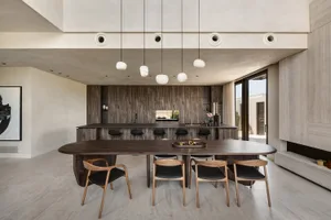 A modern dining room featuring a wooden table and chairs, set against a backdrop of a kitchen with wooden cabinets.