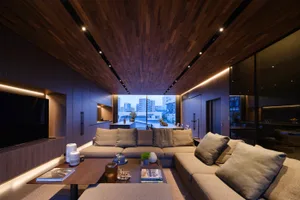 Modern living room featuring wooden elements, gray sofas, and a coffee table with books and plants.