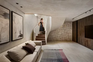 A modern living space featuring neutral materials, with a woman standing on a spiral staircase leading to another floor.