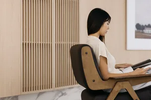 A person sitting in a modern office setting with a wooden chair and wood paneling in the background.